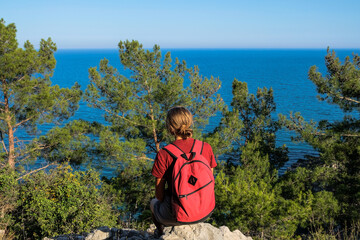 traveler girl sits on top of a mountain looks at the sea