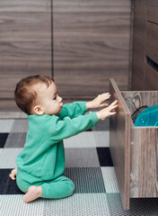 Little boy open the kitchen drawers to play with kitchenware inside. Baby exploring kitchen objects.