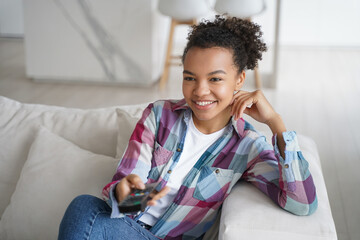 Smiling biracial young girl enjoy television program, watch TV series, sitting on couch at home