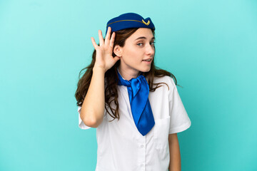 Airplane stewardess woman isolated on blue background listening to something by putting hand on the ear