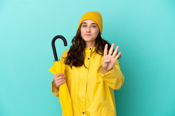 Young caucasian man holding an umbrella isolated on blue background happy and counting four with fingers