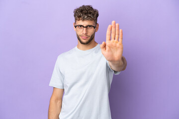 Delivery caucasian man isolated on purple background making stop gesture