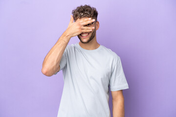 Naklejka premium Delivery caucasian man isolated on purple background covering eyes by hands and smiling