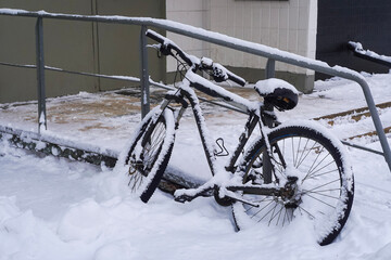 Bicycle under snow near the building entrance, winter in the city