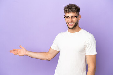 Delivery caucasian man isolated on purple background extending hands to the side for inviting to come