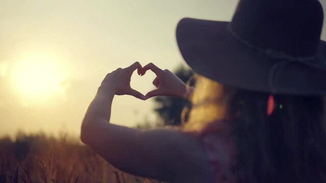 girl formed heart shape with fingers and then enjoyed sun wearing  hat