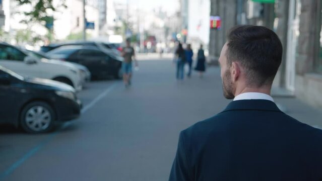 Successful male top manager goes to work, back view. Rear view handsome 30 year old top manager in classical suit walks in the city center, commuting to work. Business person concept.