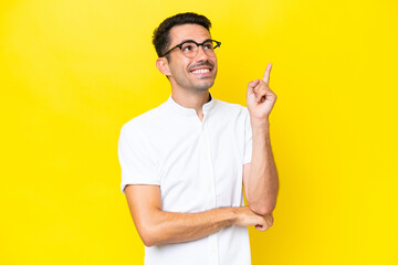 Young handsome man over isolated yellow background pointing up a great idea