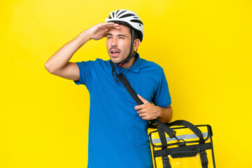 Young handsome man with thermal backpack over isolated yellow background looking far away with hand to look something