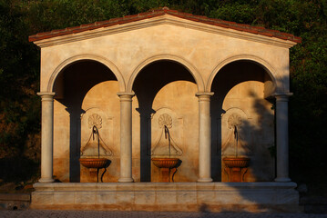 Last rays of sunlight on a spring evening. Three fountains under the arches of a wash-house,...