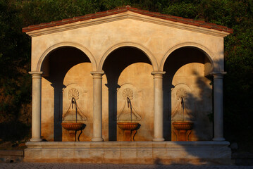 Fototapeta premium Last rays of sunlight on a spring evening. Three fountains under the arches of a wash-house, boulevard St Michel, in Lamalou-les-Bains (Hérault, France) 