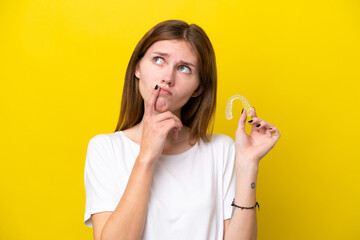 Young English woman holding invisible braces having doubts while looking up