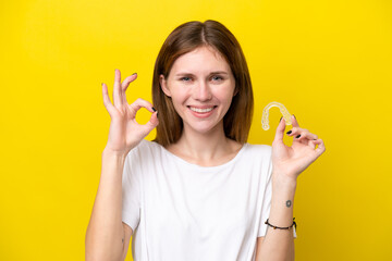 Young English woman holding invisible braces showing ok sign with fingers