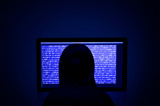 Rear view of computer hacker sitting at desk with equipment - Powered by Adobe