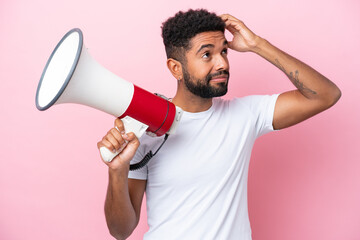 Young Brazilian man isolated on pink background holding a megaphone and having doubts