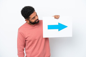 Young Brazilian man isolated on white background holding a placard with arrow symbol