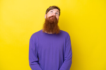 Fototapeta premium Redhead man with beard isolated on yellow background and looking up