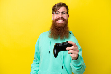 Fototapeta na wymiar Redhead man with beard playing with a video game controller isolated on yellow background with happy expression