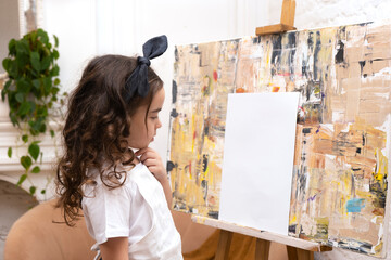 Fototapeta na wymiar Lovely girl with paintbrush is thinking about a new drawing. Little painting artist.