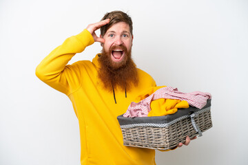 Redhead man with beard holding a clothes basket isolated on white background with surprise...
