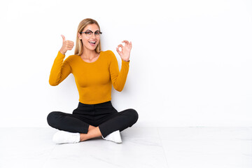 Blonde Uruguayan girl sitting on the floor showing ok sign and thumb up gesture