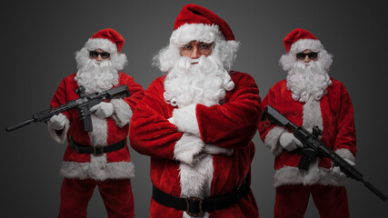 Studio shot of santa posing with crossed arms and two santa with rifles standing on his sides.