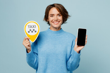 Young smiling happy cheerful caucasian woman wear knitted sweater use mobile cell phone booking taxi cab isolated on plain pastel light blue cyan background studio portrait. People lifestyle concept.