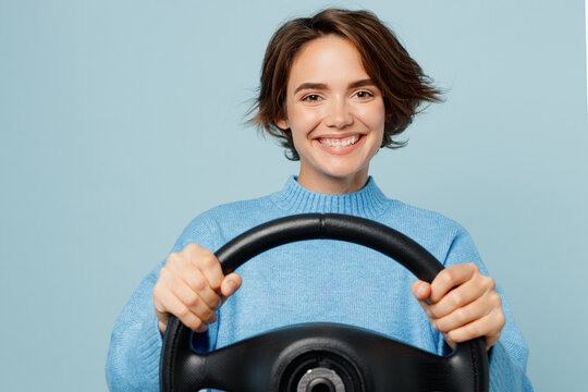 Young smiling cheerful fun caucasian woman in knitted sweater look camera hold steering wheel driving car isolated on plain pastel light blue cyan background studio portrait People lifestyle concept