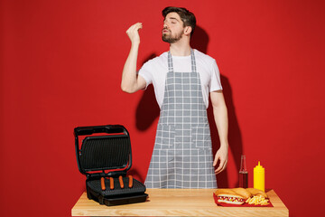 Young housekeeper chef cook baker man in grey apron work at table with grill kitchenware raised...