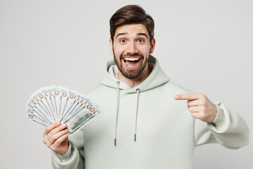 Young amazed man wear mint hoody look camera hold in hand point index finger on fan of cash money...