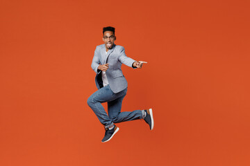 Fototapeta na wymiar Full body young employee business man corporate lawyer wearing classic formal grey suit shirt glasses work in office jump high point index finger aside on area isolated on plain red orange background.