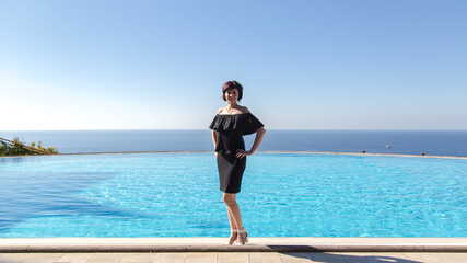 Slender brunette in a stylish black dress near the outdoor pool in the hotel.