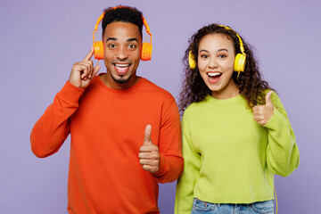 Young excited couple two friends family man woman of African American ethnicity wear casual clothes headphones listen to music together show thumb up solated on pastel plain light purple background.