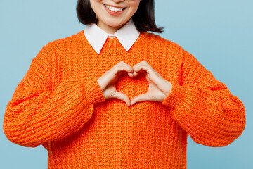 Cropped young woman of Asian ethnicity wear orange sweater glasses showing shape heart with hands heart-shape sign isolated on plain pastel light blue cyan background studio. People lifestyle concept.