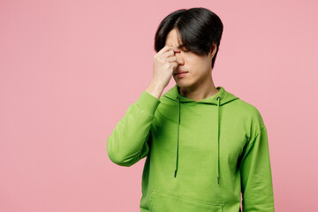 Young tired exhausted preoccupied man of Asian ethnicity wear green hoody keep eyes closed rub put hand on nose isolated on plain pastel light pink background studio portrait People lifestyle concept