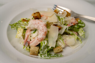 Cesar Salad with Prawns, Parmesan Shavings and Croutons and Garlic Dressing on a white Plate