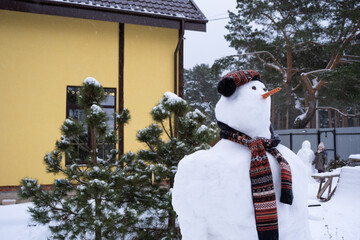 Funny snowman in a hat and scarf on the background of a yellow house in the yard. Winter, winter...
