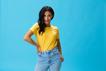 Fototapeta na wymiar Woman in yellow t-shirt on blue background posing gestures emotions and signals with smile, hands up happiness copy space