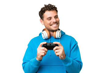 Brazilian man playing with a video game controller over isolated chroma key background looking to the side and smiling