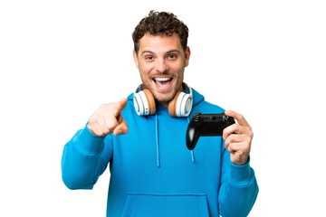 Brazilian man playing with a video game controller over isolated chroma key background surprised and pointing front © luismolinero