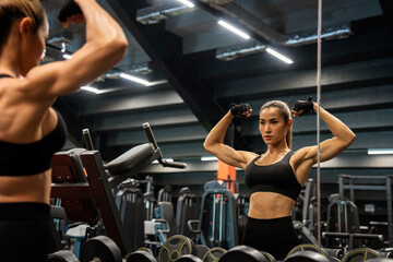 Fototapeta na wymiar Training, building muscles, workout, exercises,concept.Asian woman in fitness gloves standing in mirror looking muscular and building arm muscles looking strong and powerful in gym 