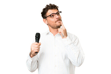 Naklejka premium Brazilian man picking up a microphone over isolated chroma key background having doubts while looking up