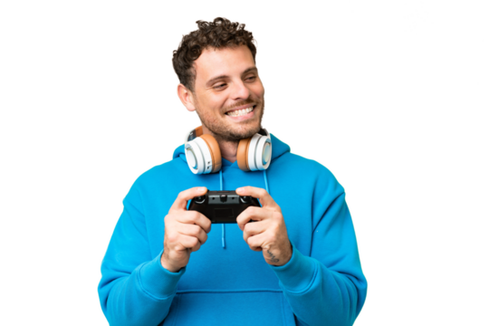 Brazilian man playing with a video game controller over isolated chroma key background looking to the side and smiling