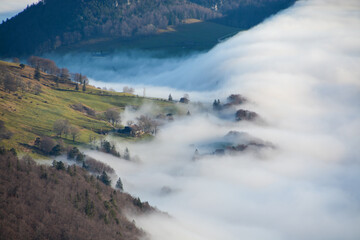 Beautiful view of fog climbing up the hill and capturing trees and houses behind a white soft...