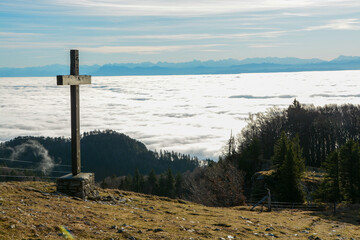 Panoramic view of the swiss alps above a see of fog with a wooden peak-cross in the foreground from Röti peak in Solothurner Jura, Switzerland