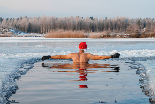 Young man in Santa's hat swimming in an ice cold water surrounded by ice. Cold swims for health. 