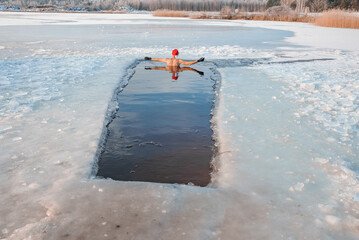 Young man in Santa's hat swimming in an ice cold water surrounded by ice. Cold swims for health. 