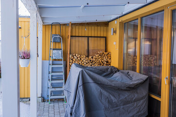 Obraz na płótnie Canvas Beautiful view of backyard of private house on winter day with birch firewood stack, with summer furniture under cover. Sweden.