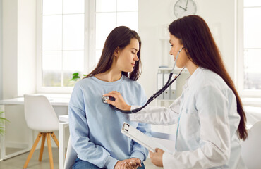 Female doctor listens to patient's breathing by applying stethoscope to her chest. Doctor listens...
