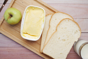 fresh butter in a container with bread, apple and milk on table 